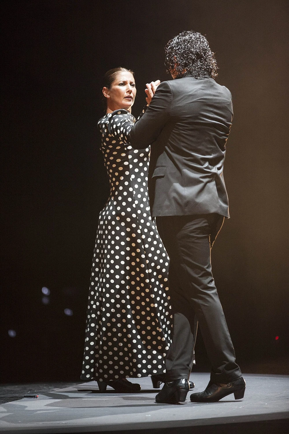 Sara Baras in a black dress with white polka dots, dancing on stage opposite another dancer.