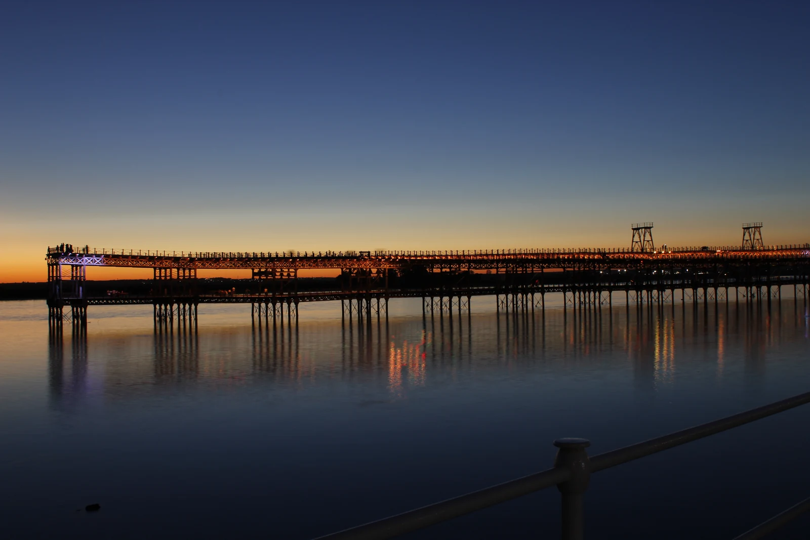The iron structure of the Muelle del Tinto in Huelva reflected in the water at dusk.