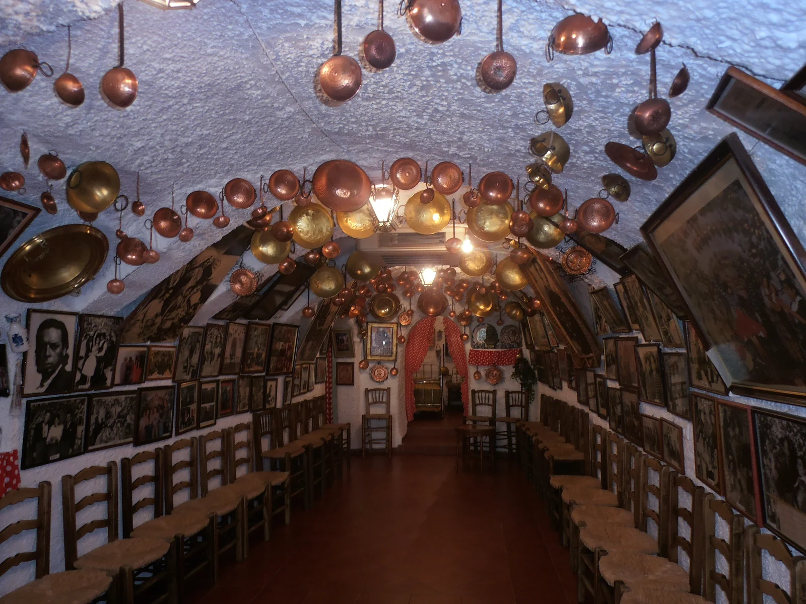 Interior of María la Canastera in Granada, with chairs along the cave walls and copper pans suspended from the ceiling.