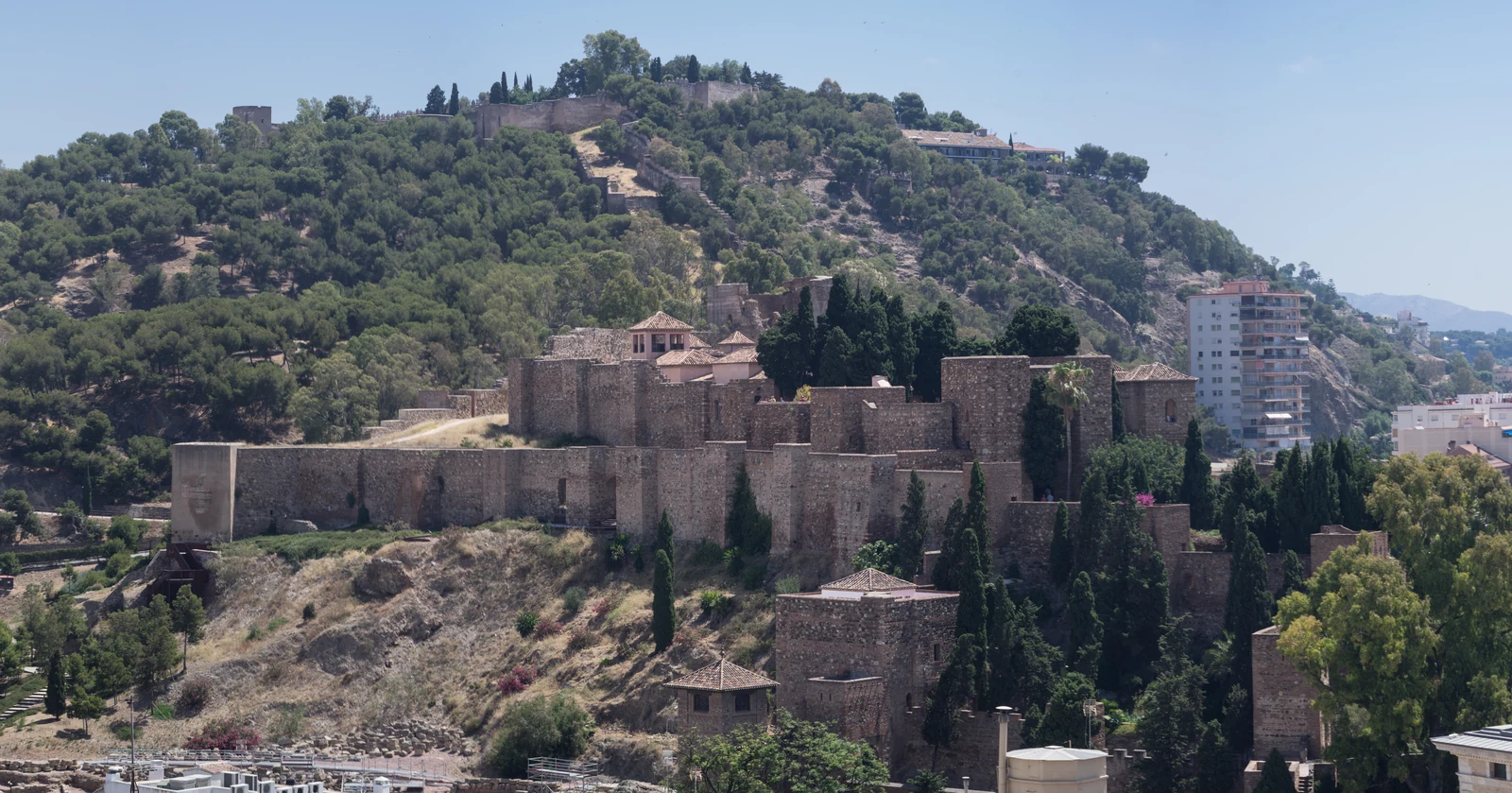 Stone towers and walls of the Alcazaba of Málaga against the wooded hillside, seen from the cathedral.